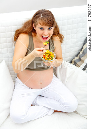 Smiling beautiful pregnant woman sitting on couch and eating fruit salad. Smiling beautiful pregnant woman sitting on couch and eating fruit salad. 14792967