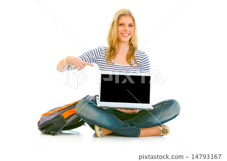 Smiling teengirl sitting on floor with schoolbag and pointing finger on laptop with blank screen. 14793167