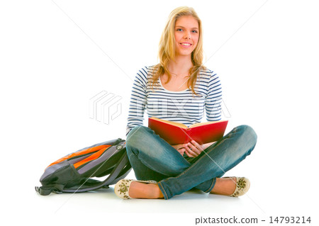 Smiling teen girl with backpack sitting on floor and reading sch 14793214