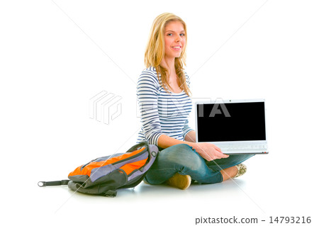 Smiling teen girl sitting on floor and showing laptops blank scr 14793216