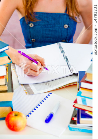 Girl sitting at table with lots of books and doing homework. Close up. 14793231