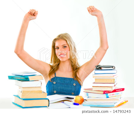 Pleased young girl with raised hands sitting at desk with books. Pleased young girl with raised hands sitting at desk with books. 14793243