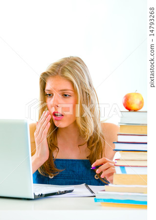 Shocked teen girl sitting at table with books and looking on laptop . 14793268
