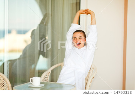 Beautiful woman in bathrobe sitting at table on terrace and stre Beautiful woman in bathrobe sitting at table on terrace and stre 14793338