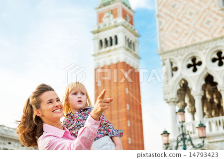 Happy mother pointing baby on something while standing against c Happy mother pointing baby on something while standing against c 14793423