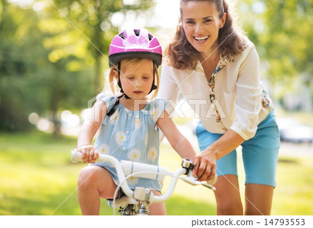 Happy mother helping baby girl riding on bicycle Happy mother helping baby girl riding on bicycle 14793553