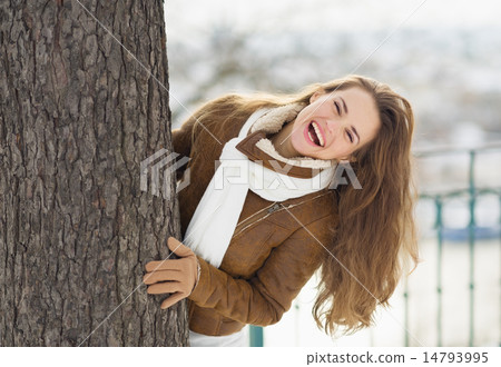 Happy young woman looking out from tree Happy young woman looking out from tree 14793995