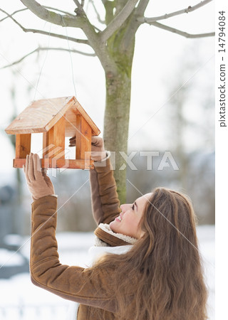 Happy young woman adding meal into bird feeder Happy young woman adding meal into bird feeder 14794084