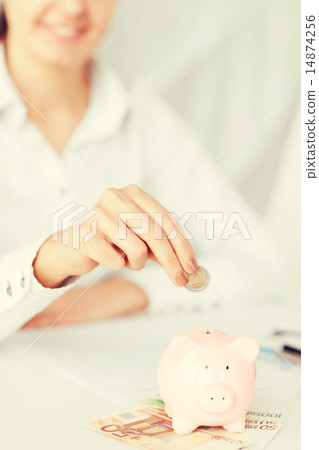 woman hand putting coin into small piggy bank woman hand putting coin into small piggy bank 14874256