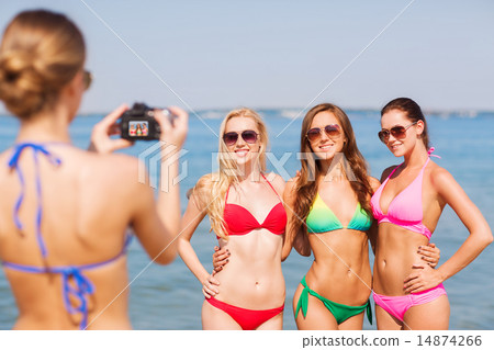 group of smiling women photographing on beach 14874266