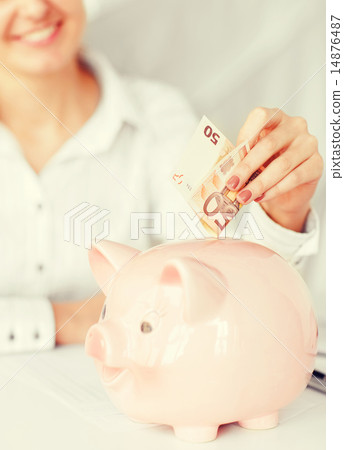 woman puts euro cash into large piggy bank woman puts euro cash into large piggy bank 14876487