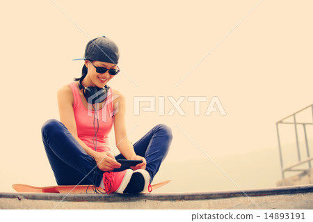 woman skateboarder listening music from cellphone woman skateboarder listening music from cellphone 14893191