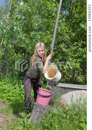 young woman at a well, pours water in a bucket.. young woman at a well, pours water in a bucket.. 14968201