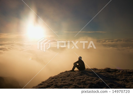 Tired hiker in black sit on frozen grass on hill Tired hiker in black sit on frozen grass on hill 14970720