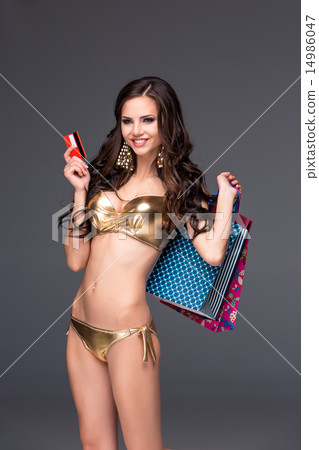 Pretty woman in gold bikini holding shopping bags and showing blank credit card Pretty woman in gold bikini holding shopping bags and showing blank credit card 14986047
