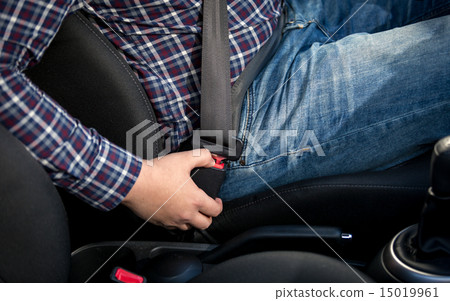 Closeup photo of man seating on drivers seat and fastening belt 15019961
