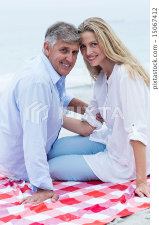 Happy couple sitting on a blanket and smiling at camera Happy couple sitting on a blanket and smiling at camera 15067412