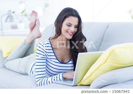 Smiling beautiful brunette relaxing on the couch and using her l 15067941