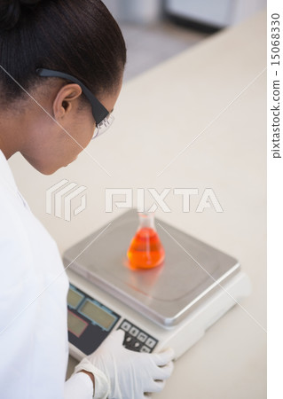 Scientist weighing beaker with orange fluid inside 15068330