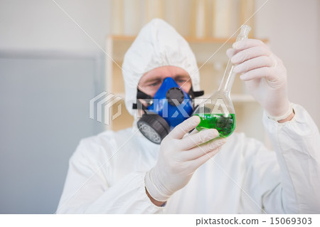 Scientist in protective suit examining green precipitate 15069303