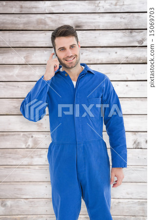 Composite image of smiling male mechanic using mobile phone 15069703