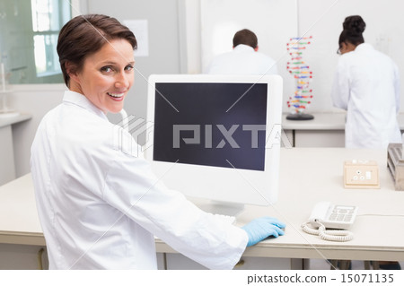 Smiling scientist using computer while colleagues working 15071135