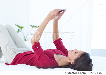 Beautiful woman using her smartphone lying on bed 15071369