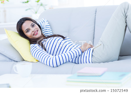 Smiling beautiful brunette relaxing on the couch and looking at 15072549