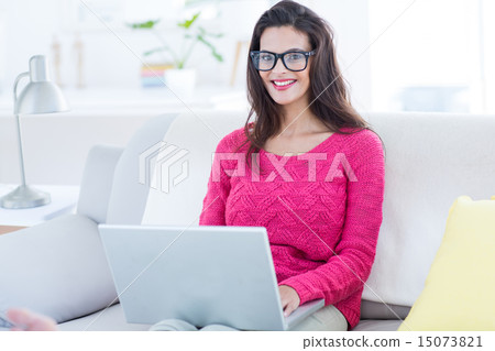Smiling beautiful brunette using her laptop on the couch Smiling beautiful brunette using her laptop on the couch 15073821