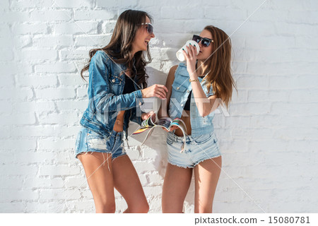 two pretty girls wearing sunglasses in summer jeanswear street urban casual style talking, laughing  15080781