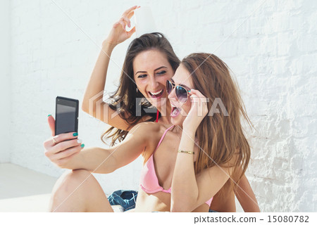 Female friends laughing having fun taking selfie together wearing bikini bra swimsuit summer sunny d Female friends laughing having fun taking selfie together wearing bikini bra swimsuit summer sunny d 15080782