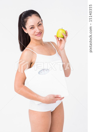 Smiling brunette holding weighing scales and apple Smiling brunette holding weighing scales and apple 15140355