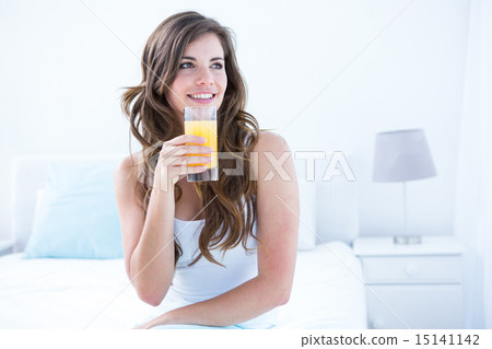 Thoughtful brunette drinking a glass of orange juice 15141142
