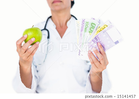 Confident female doctor holding green apple and banknotes 15141457
