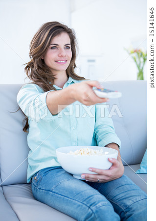 Happy brunette watching television with bowl of popcorn 15141646