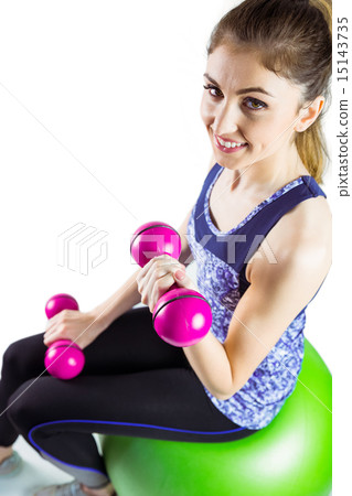Fit woman lifting dumbbell sitting on ball 15143735
