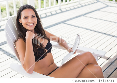 Pretty brunette sitting on a chair and reading magazine Pretty brunette sitting on a chair and reading magazine 15143834