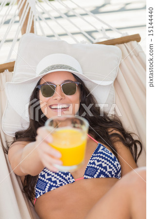 Pretty brunette relaxing on a hammock and drinking orange juice 15144440