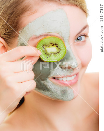 Woman in clay mask on face covering eye with kiwi 15147557