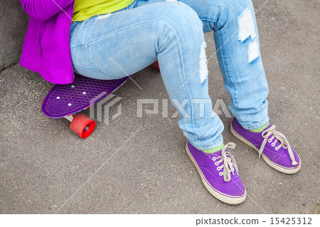 Teenager in jeans and gumshoes sits on skateboard 15425312