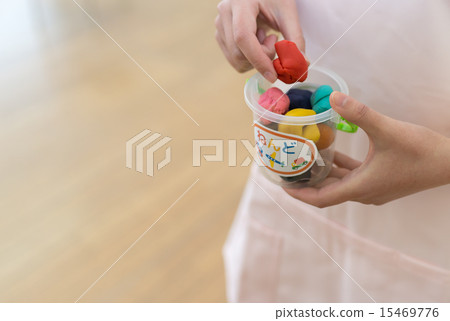 A nursery teacher putting colorful wheat clay into a container. A nursery teacher putting colorful wheat clay into a container. 15469776