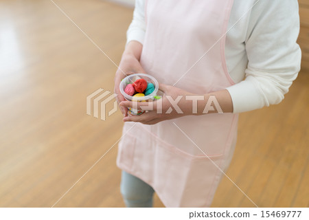 一位身穿圍裙的幼兒園老師手持一罐小麥黏土。 15469777