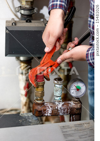 Closeup of plumber turning heating system valve with red pliers 15481026