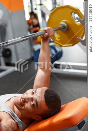 Lying man lifting barbell in gym  15510610