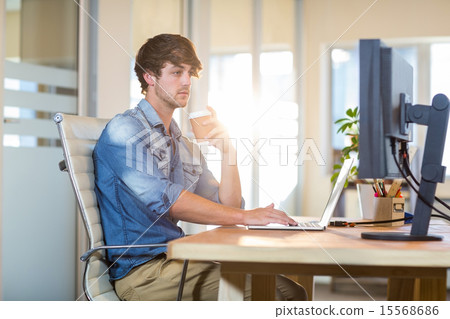 Serious casual businessman sitting at desk Serious casual businessman sitting at desk 15568686