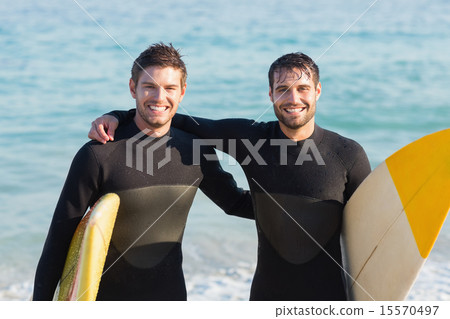 Two men in wetsuits with a surfboard on a sunny day Two men in wetsuits with a surfboard on a sunny day 15570497