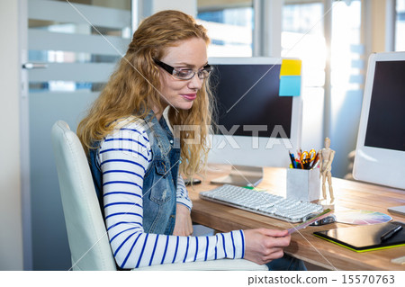 Smiling designer sitting at her desk and looking at colour swatc Smiling designer sitting at her desk and looking at colour swatc 15570763