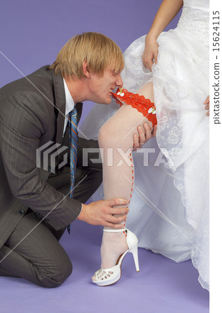 Amusing groom removes a garter from leg of bride 15624115