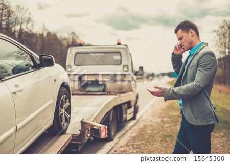 Man calling while tow truck picking up his broken car 15645300