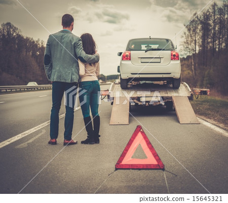 Couple near tow-truck picking up broken car 15645321